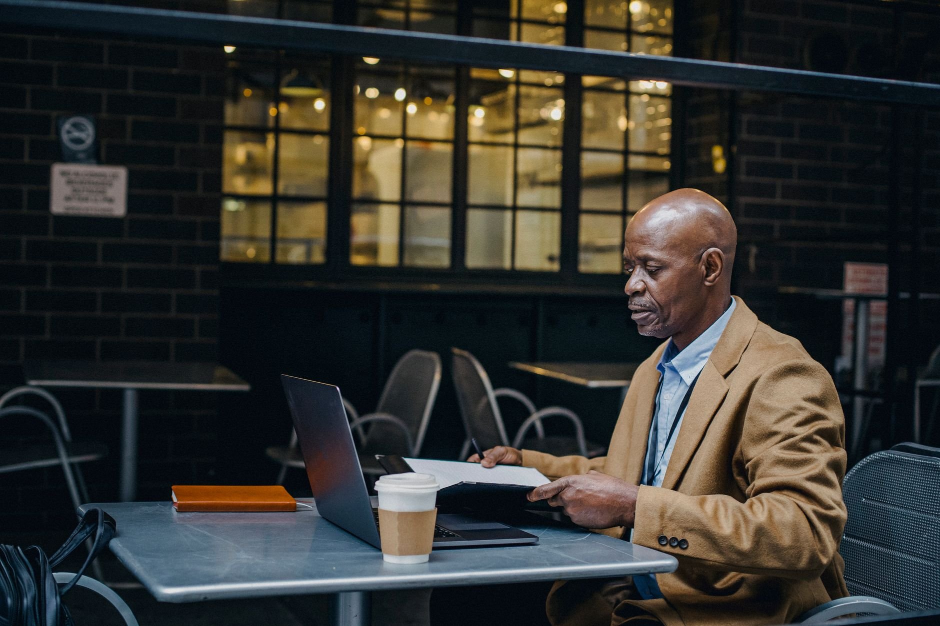 Entrepreneur reading and working on a laptop in a city cafe — the focused daily work of growing a newsletter